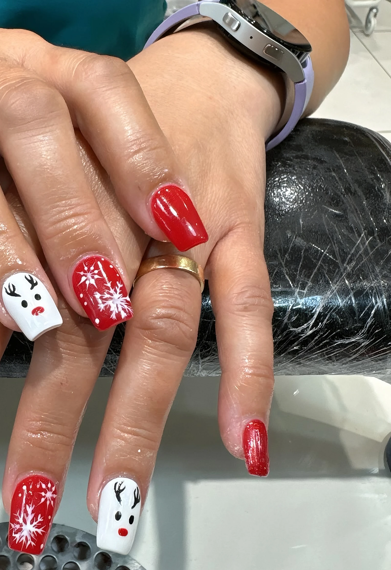 Red Christmas nails with snowflakes and reindeer, done at the salon desk
